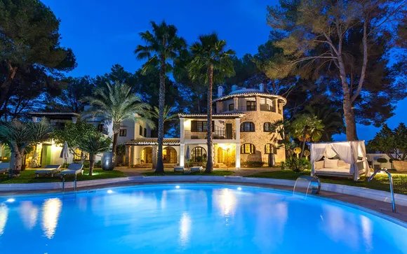Can Talaia lit at dusk behind the pool and palms